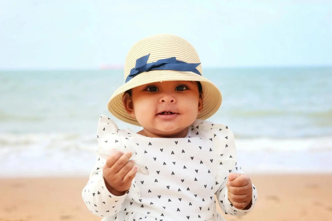 Bébé sous le soleil à la plage avec des habit anti-UV et un chapeau 